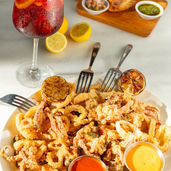 Fried calamari with sauces, sangria, empanadas, and lemons on a white table.