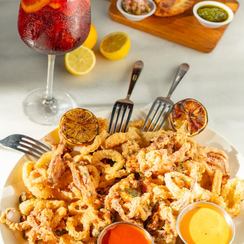 Fried calamari with sauces, sangria, empanadas, and lemons on a white table.