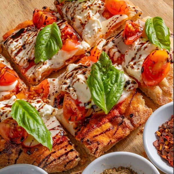 Close-up of a sliced flatbread pizza with tomatoes, mozzarella, basil, and balsamic glaze.