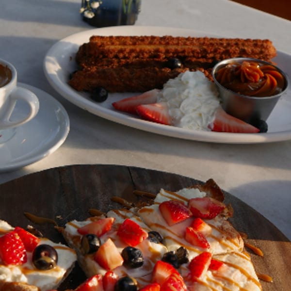Churros with whipped cream and strawberries, alongside a flatbread with berries and caramel drizzle.