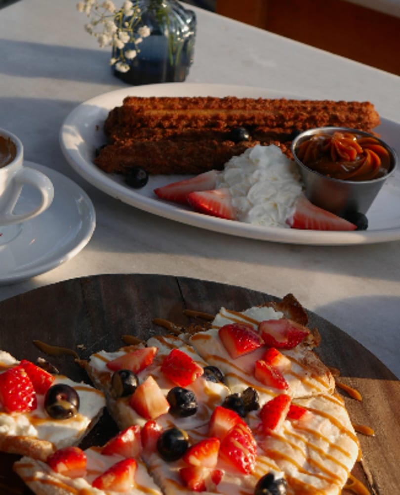Churros with whipped cream and strawberries, alongside a flatbread with berries and caramel drizzle.